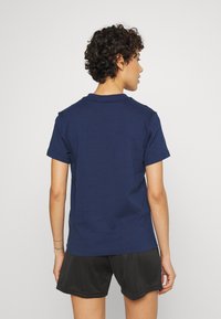 T-shirt en coton bleu marine avec un col rond et des manches courtes, vue de dos, assortie à un short de sport noir.