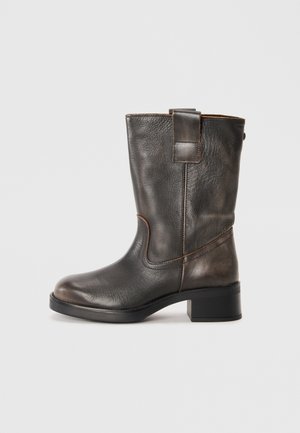 Brown leather ankle boot with a rounded toe, subtle stitching, a decorative pull-tab, and a low block heel. Smooth texture, minimal design.