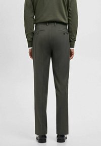 Man wearing dark green dress pants and matching sweater, standing with hands at sides, shown from the back against a plain background.