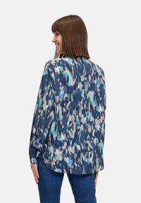 Blouse in blauw en teal met een patroon, met een losse pasvorm, lange mouwen en een ronde zoom, gemaakt van een lichte stof.
