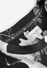 Čierne tričko s kvetinovým vzorom v šedej a bielej farbe. Okrúhly výstrih s textúrovaným lemovaním. Štítok uvádza "od Ted Baker London," veľkosť 12.