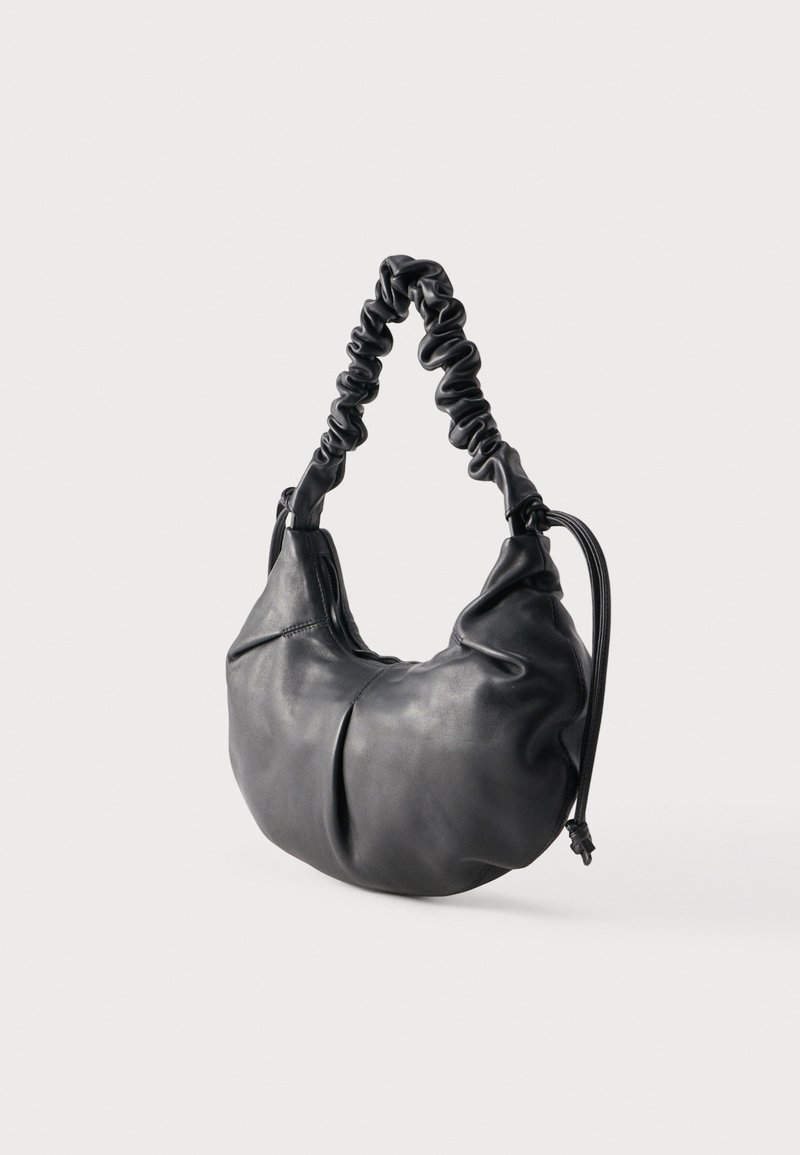 Sac à main en cuir noir souple avec une bandoulière froncée et un corps arrondi et décontracté sur un fond uni.