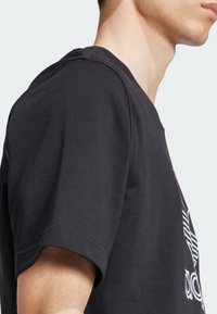 T-shirt in cotone nero con maniche corte, collo rotondo e cuciture visibili. Presenta un design del logo bianco sul fronte.