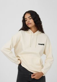 Kremowa bluza z kapturem, z przednią kieszenią i sznurkiem. Wyróżnia się czarnym napisem "CRIME". Wykonana z miękkiego materiału, luźny krój, długie rękawy.
