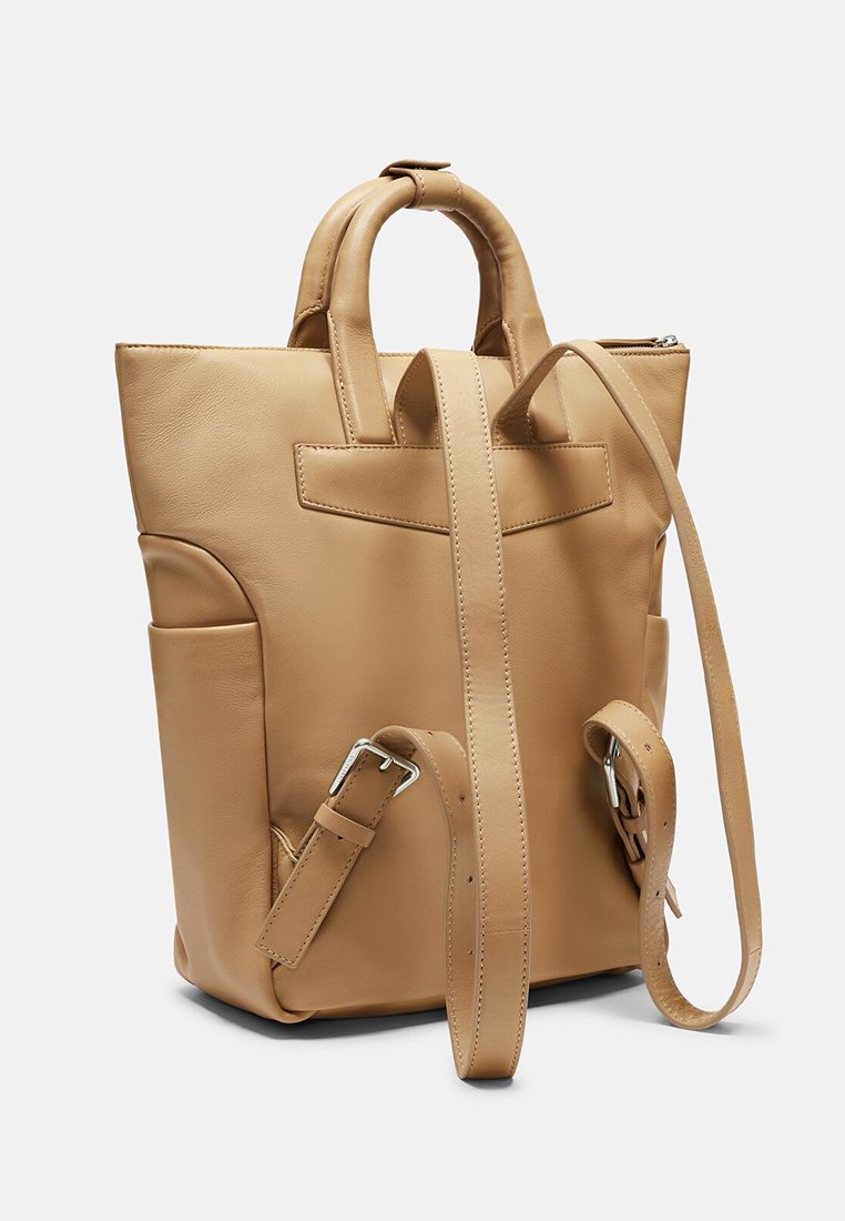 Brauner Leder-Rucksack mit zwei Griffen, verstellbarem Riemen, Fronttasche und minimalistischem Design; glatte Textur mit dezenten Nähten.