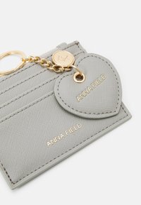 Gray faux leather cardholder with gold-tone hardware, featuring a heart-shaped tag and vertical stitching. "ANNA FIELD" embossed in gold.