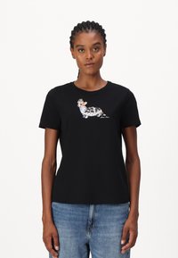 Zwarte katoenen t-shirt met een grafisch ontwerp van een Corgi met bloemdessins. Ronde hals en korte mouwen. G gedragen met blauwe jeans.