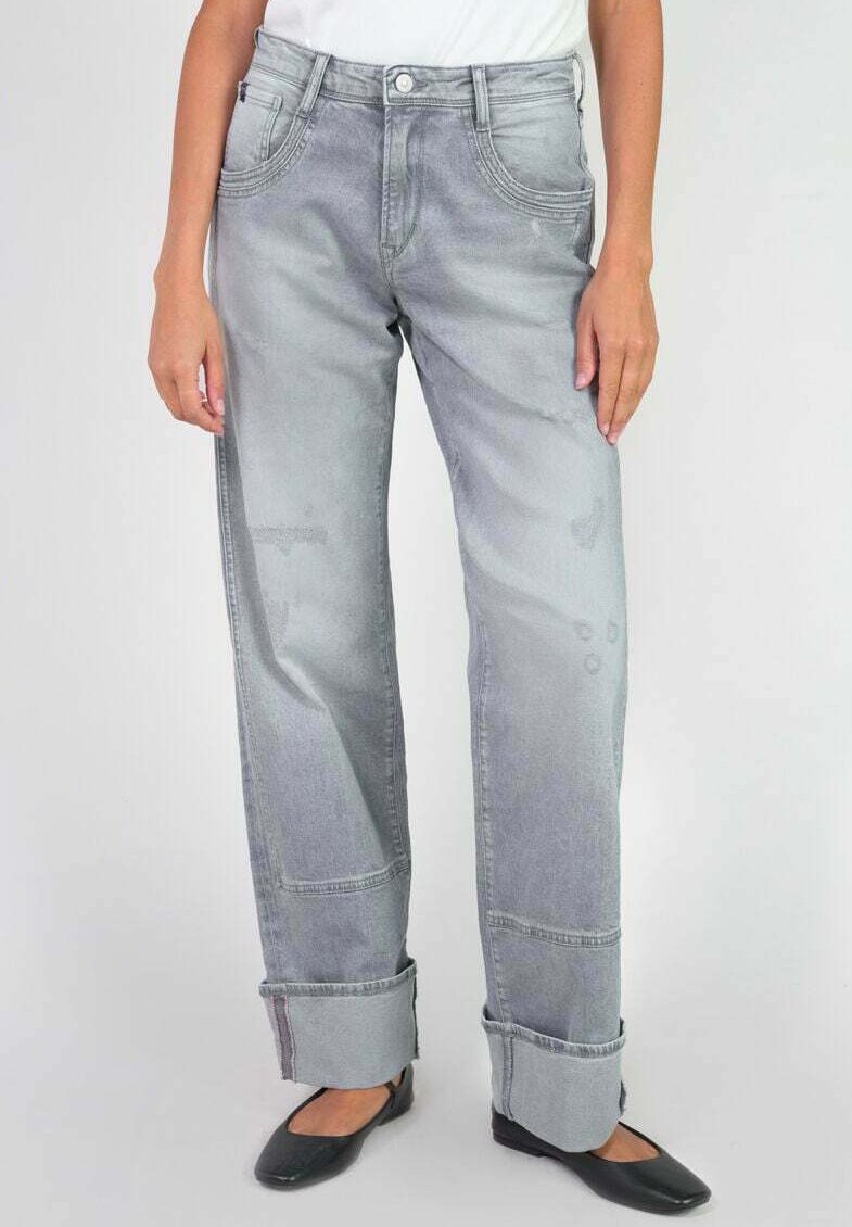 Jeans en denim gris clair avec une coupe ample, présentant des coutures visibles, des détails usés et des ourlets retroussés. Portés avec des chaussures noires plates.
