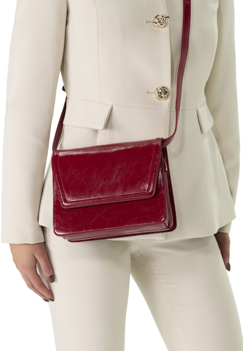 Rote Leder-Crossbody-Tasche mit rechteckiger Form, Klappverschluss und schmalem Riemen, mit glänzender Oberfläche und subtiler Textur.