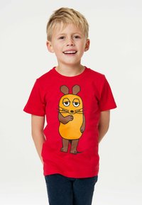 Rotes kurzärmliges T-Shirt mit einem Cartoon-Charakter, der einen orangefarbenen Körper, braune Akzente und übertriebene Gesichtszüge hat, kombiniert mit blauen Jeans.