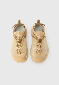 Μπεζ αθλητικά παπούτσια με ανώτερο μέρος από τούλι και συνθετικά υλικά, στρογγυλή μύτη, υφή στην σόλα και σύστημα κορδονιών. Διαθέτουν θηλιά στο πίσω μέρος.