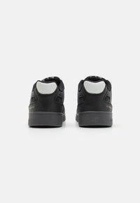 Sorte skinnesneakers med en glatt finish, hvite detaljer på hælen og en teksturert grå såle. Har preget merkevarelogo på siden.