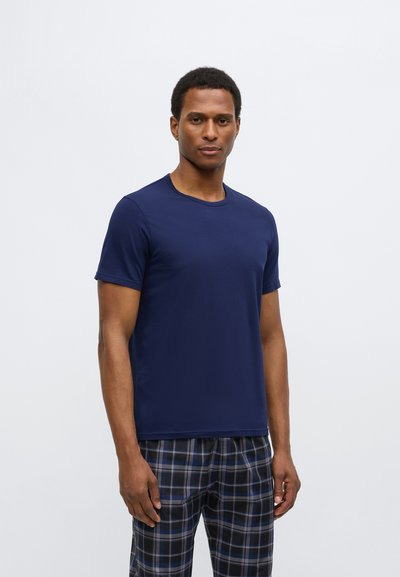 Tumši zils īsroku T-krekls no gludas auduma ar apaļu kakla izgriezumu, kombinēts ar rūtainām biksēm zilās un pelēkās toņos.