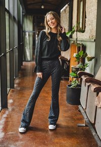 Zwarte, gestructureerde lange mouw top, gecombineerd met hoge taille, flare broek met een golvend patroon. Zwart-witte sneakers maken de look af.