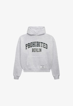 Mand iført en grå hættetrøje med teksten "PROHIBITED BERLIN", en sort baseballkasket og bukser med nålestriber mod en ensfarvet lys baggrund.
