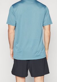 Kurzärmeliges, hellblaues Sportshirt aus glattem Stoff, kombiniert mit dunklen Shorts. Das Shirt verfügt über einen klassischen Kragen und einen lässigen Schnitt.