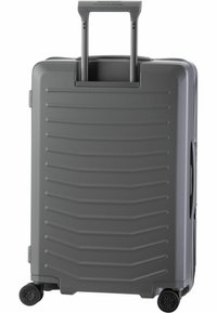 Maleta rígida gris con una superficie texturizada, mango retráctil y cuatro ruedas para mayor movilidad. Presenta estrías horizontales y asas laterales.