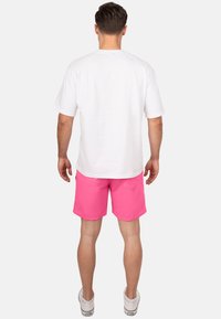 Tenue masculine composée d'un t-shirt en coton blanc uni et de shorts roses brillants. Les shorts ont un design simple avec une poche arrière, portés avec des baskets blanches.