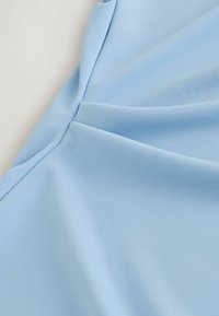 Lyseblåt stof med en glat tekstur, der har subtile plisseringer og et struktureret design. Den bløde fald giver stoffet en smuk form.