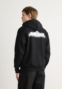 Sudadera negra con un estampado texturizado en la parte posterior que presenta el horizonte de Copenhague y estrellas. Tejido suave, capucha con cordón y puños acanalados.