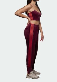 Burgundy sammetstopp som slutar vid midjan och matchande joggers med röda ränder, kompletterat med ljusa sneakers. Har elastisk midja.