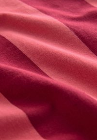 Weicher Stoff mit abwechselnd breiten Streifen in Dunkelrot und Hellrosa, der subtile Falten und Textur im Nahbereich zeigt.