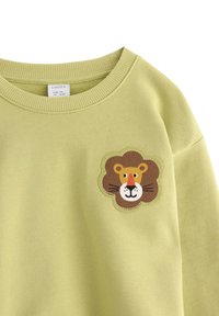 Felpa per bambini di colore verde chiaro con una toppa a forma di faccia di leone marrone sul petto, scollo rotondo e colletto a costine.