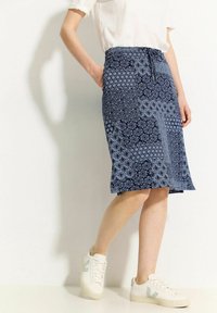 Modrá sukně s potiskem a elastickým pasem, zdobená květinovými a geometrickými vzory. Spárována s bílými teniskami s zelenými akcenty.