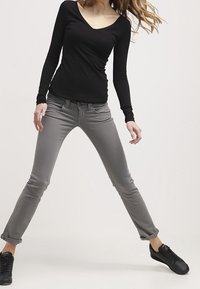 Grå slim-fit jeans med en mjuk textur och framfickor, kombinerat med en svart långärmad topp. Svarta sneakers fulländar looken.