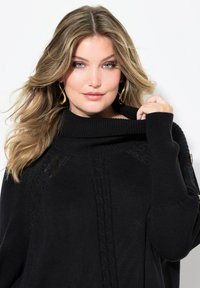 Pull noir en tricot avec un col cheminée, présentant des détails en tricot torsadé et une coupe ample. Accentué par un bouton à l'épaule.