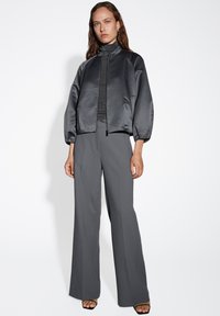 Giacca corta in satin con colletto rialzato, di colore grigio, e polsini a coste. Abbinata a pantaloni sartoriali grigi larghi e sandali neri con tacco.