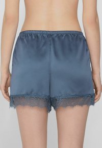 Satin slaapshorts in diepblauw met een geschulpte kanten rand aan de zoom. Elastische tailleband voor comfort. Glad textuur overal.