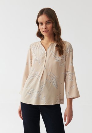 Blouse beige clair avec décolleté en V, à manches trois-quarts et motif floral gris. Tissu doux avec des détails de boutons au niveau du col.