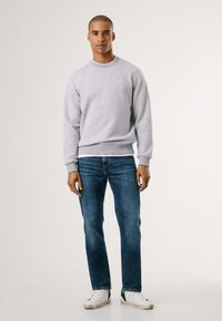 Sudadera gris con puños y dobladillo de canalé, combinada con jeans azules y zapatillas blancas con detalles verdes. Diseño sencillo, cuello redondo.