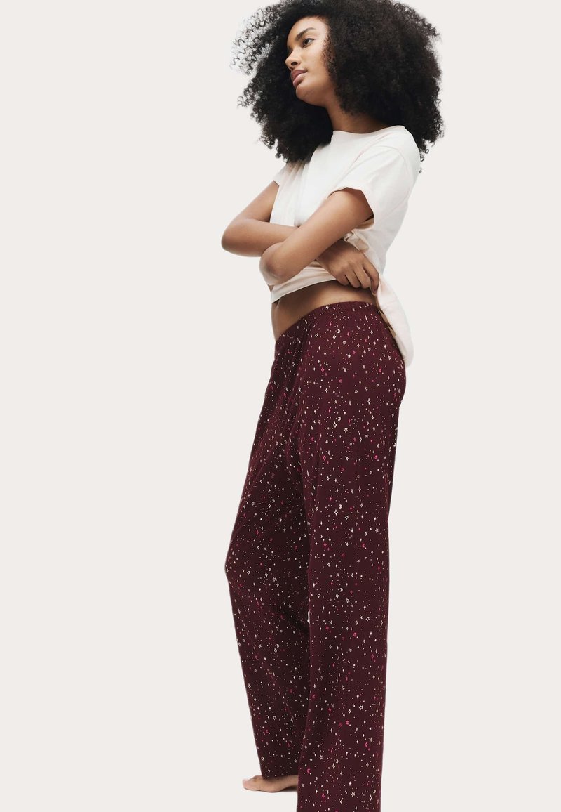 Pantalones de pijama burdeos con un corte holgado, decorados con un patrón disperso de manchas blancas y rosas. Combinados con una camiseta blanca ajustada de manga corta.
