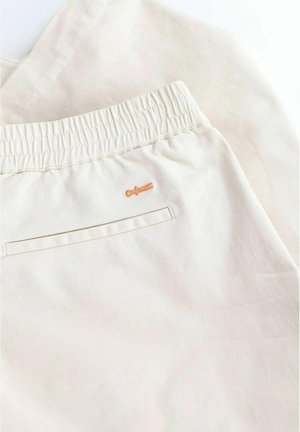 Beige bomullsshorts med elastisk midja, platt bakficka och en liten broderad orange logotyp på vänster sida.