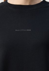 T-shirt noir à col rond avec un petit logo gris « Marc O’Polo DENIM » centré sur la poitrine.