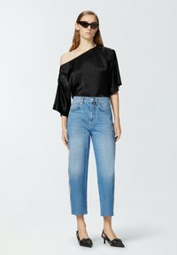 Crni satenasti top bez naramenica, svijetloplave hlače visokog struka, crne cipele s oštrim vrhom i kutne crne sunčane naočale. Glatke teksture i suvremeni dizajn.