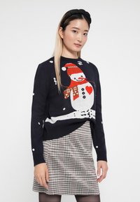 Navy knitted sweater featuring a white snowman with a red hat and scarf, accented by snowflake patterns, paired with a plaid skirt.