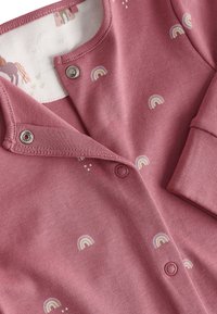 Grenouillère en coton rose ornée d'une broderie arc-en-ciel, avec des pressions et une texture douce. Comprend un design contrastant au niveau de l'encolure intérieure.