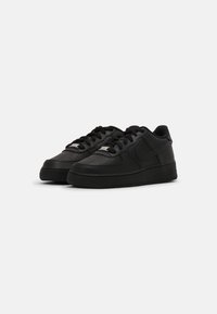Svarta sneakers med en slät läderöverkant, perforerat tåområde, texturerad sula och svarta snören. Har en elegant design och subtila varumärkesdetaljer.