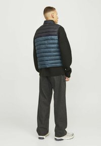 Vesta puf în navy închis și teal, cu un design matlasat orizontal. Asortată cu un pull negru texturat și pantaloni largi gri închis.