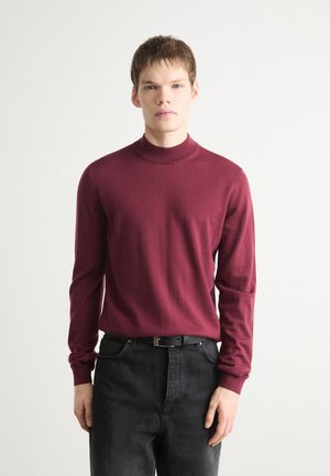 Burgundy long-sleeve turtleneck sweater in lightweight fabric. Slim fit with ribbed neckline and cuffs, paired with black jeans and a belt.