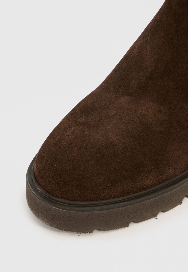 Botín de ante marrón con punta redonda, superficie texturada y suela gruesa de goma negra. Destaca por su color intenso y acabado suave.