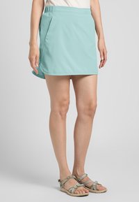 Ein hellblaues, knielanges Skort mit einem elastischen Bund und seitlichen Taschen. Getragen mit braunen Sandalen mit Riemen und einer strukturierten Sohle.