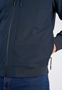 Granatowa kurtka zip-up wykonana z gładkiego materiału, z elastycznymi mankietami i dołem, z bocznymi kieszeniami oraz małym detalem z zamkiem błyskawicznym na dolnym brzegu.