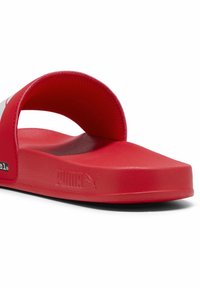 Tongs rouges en matériau synthétique. Présentent une large lanière courbée et une semelle plate avec une surface texturée. Le logo de la marque est visible.