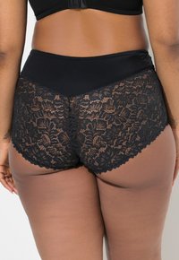 Zwarte kant hoge taille slip met een gladde tailleband en ingewikkelde bloemenpatronen aan de achterkant, met golvende randen voor een delicate afwerking.
