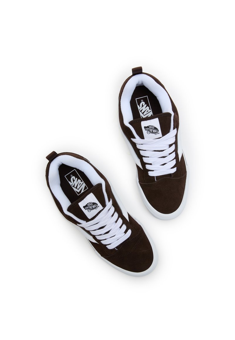 Des baskets en suede marron avec des lacets blancs, un col rembourré et une semelle en caoutchouc blanche. Logo Vans visible sur la languette et les accents latéraux.