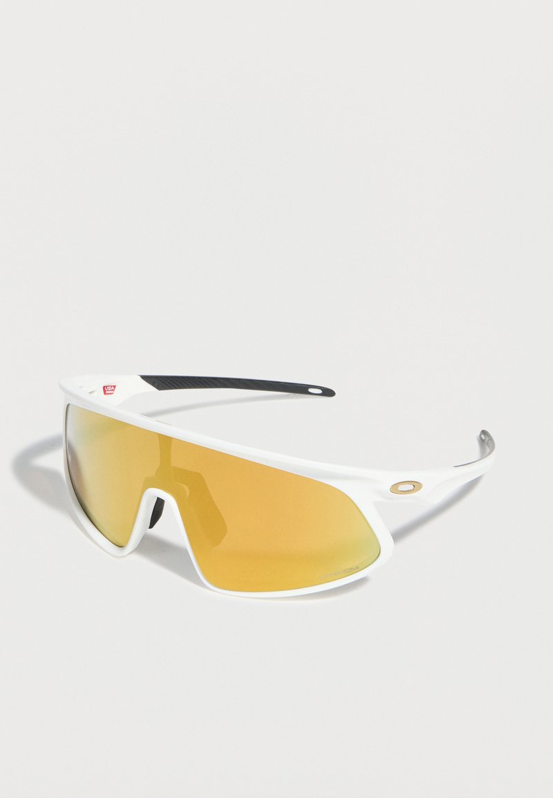 Λευκά αθλητικά γυαλιά ηλίου με περιμετρικούς φακούς με κίτρινη απόχρωση και μαύρες ελαστικές λαβές στους βραχίονες, τοποθετημένα σε ανοιχτή επιφάνεια.
